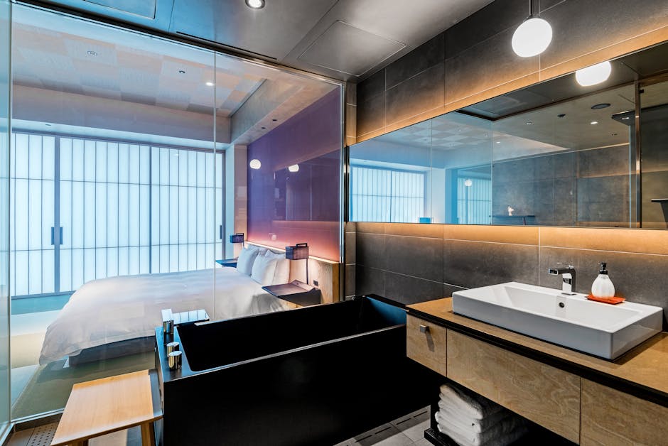 Elegant hotel bathroom with a glass door view into a stylish bedroom, showcasing luxury interiors.