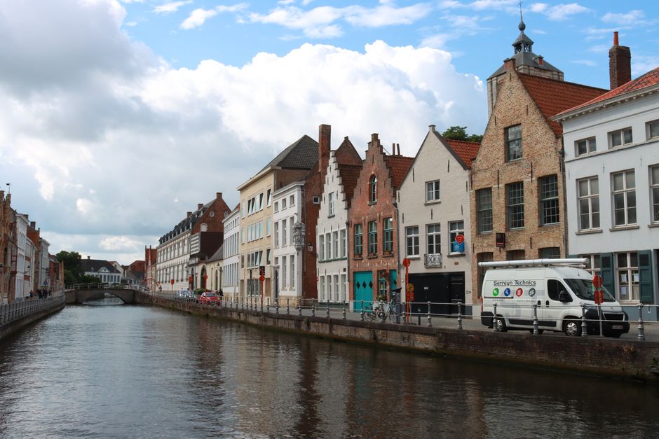 Picturesque view of Bruges' canal lined with historic buildings under a cloudy sky.