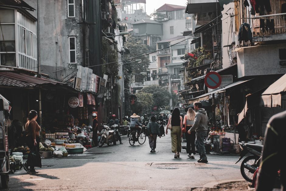 Bustling Hanoi street with people, shops, and motorbikes on a lively day.