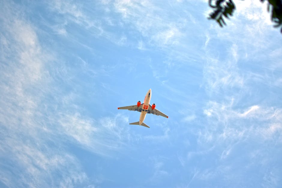 Low-angle view of airplane in flight against a blue sky with wispy clouds.
