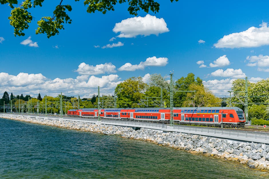 Red train traveling along Lake Constance with lush greenery.