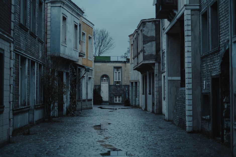 Empty paved wet alley between aged stone residential houses with windows located against overcast sky and trees in district of town