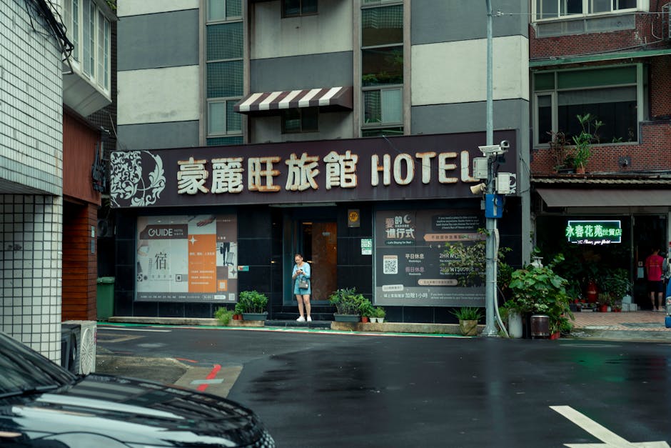 Street view of an urban hotel entrance with a person standing outside on a rainy day.