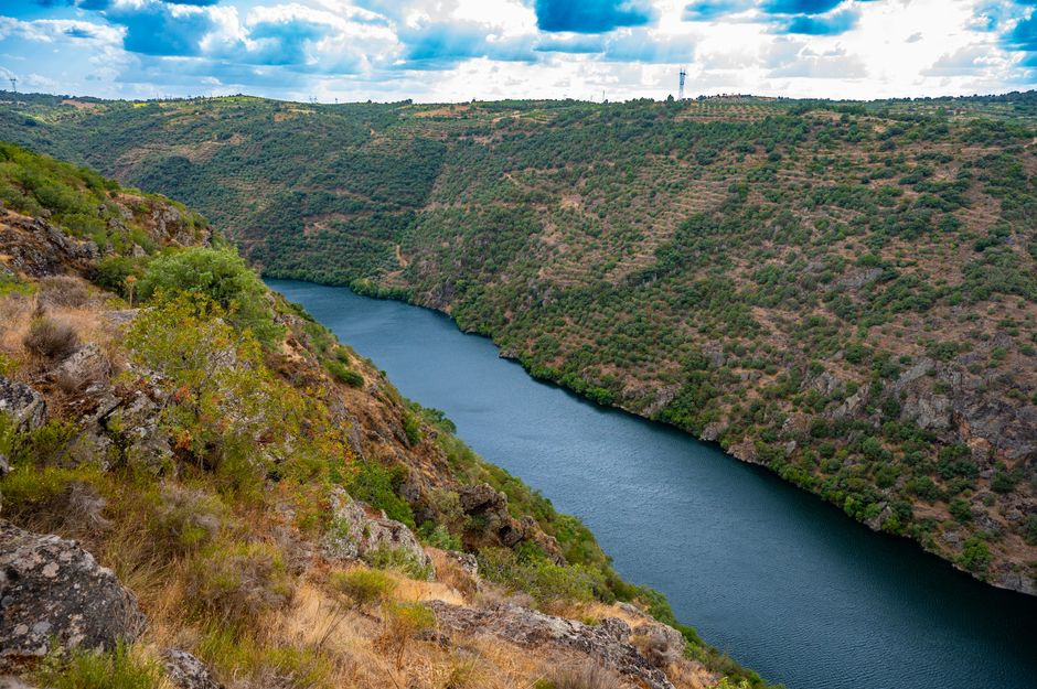 Breathtaking view of a river gorge with lush green cliffs and dramatic clouds in the sky.