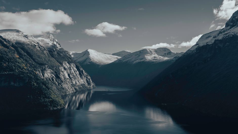 Beautiful view of a Norwegian fjord surrounded by snow-capped mountains and calm waters under a clear sky.