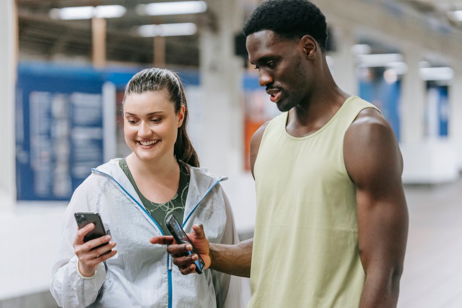 Two young adults in sports clothing sharing social media on a smartphone at a subway station.
