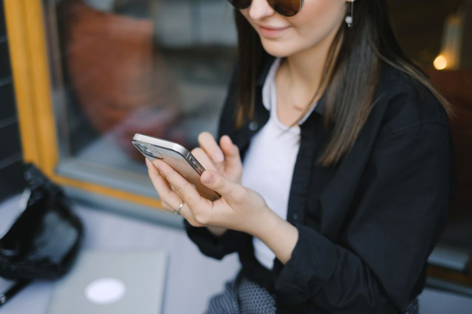 A stylish woman using her smartphone while sitting indoors by the window.