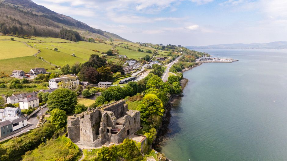 Aerial shot of historic castle ruins along the coastline of Carlingford, Ireland with lush green landscape.