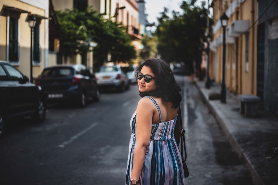 Woman wearing sunglasses and summer dress walking down a city street, creating a vibrant urban scene.