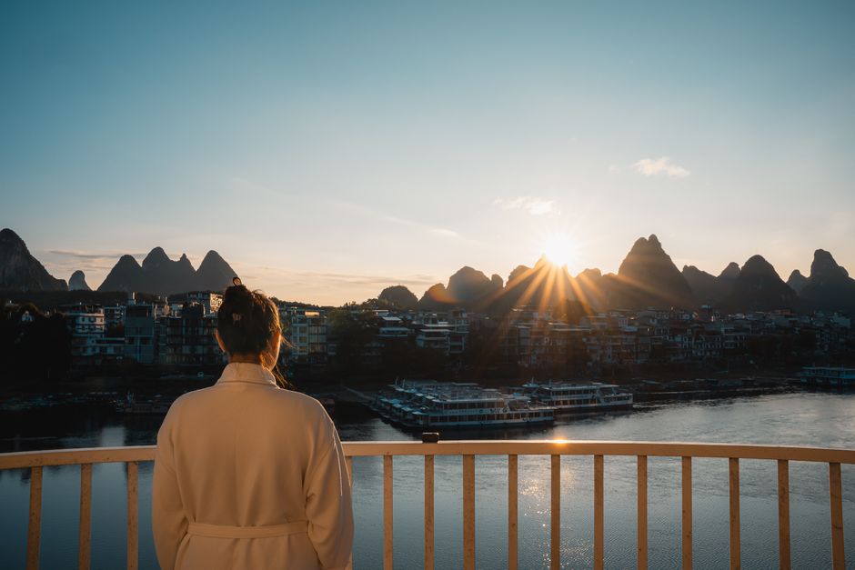 A woman enjoys a serene sunrise view of Guilin's famous karst mountains from a balcony.