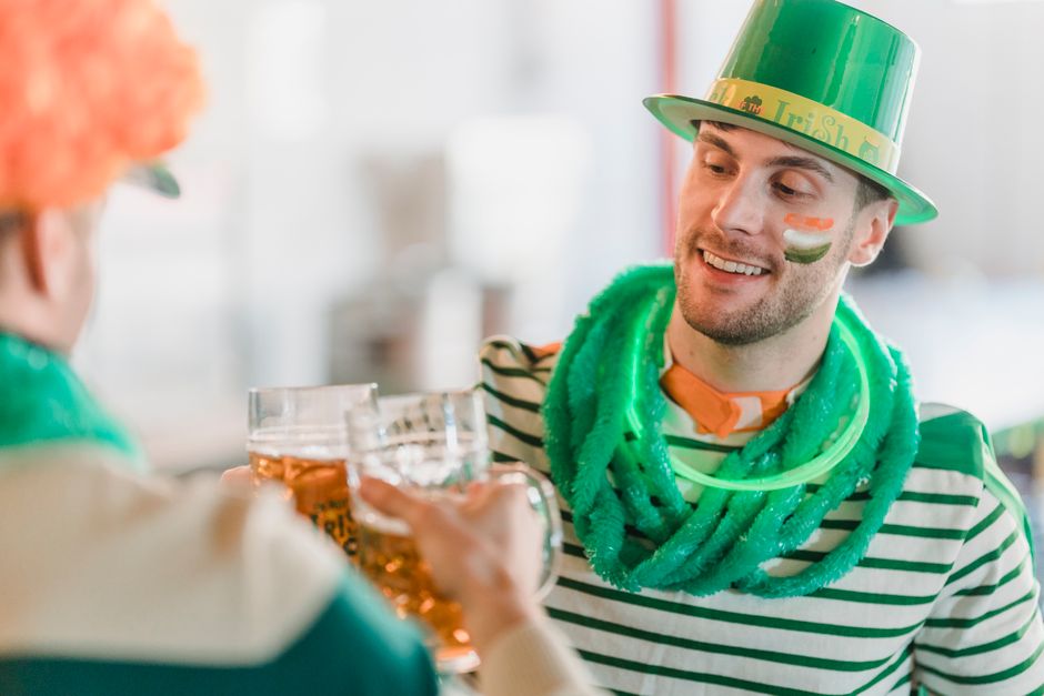 Happy men in traditional St Patricks day clothes having glasses of fresh beer on blurred background