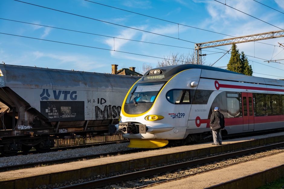 A modern train at a station while a passenger boards on a sunny day.