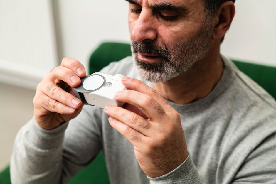 Adult man examining a medical device indoors, focused on health monitoring.