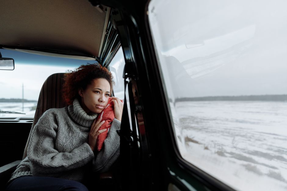 Woman in gray sweater looks out van window at snowy landscape during a winter road trip.