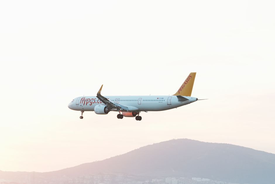 A Pegasus Airlines plane flying over a hillside in Istanbul at sunset.