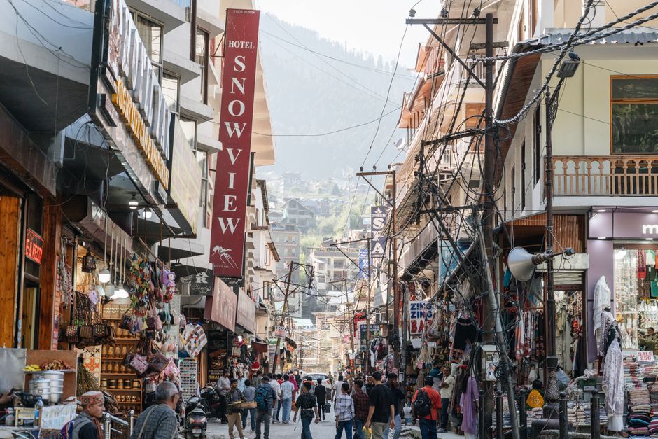 Vibrant street market in Manali, India showcasing local shops and bustling crowds under clear skies.
