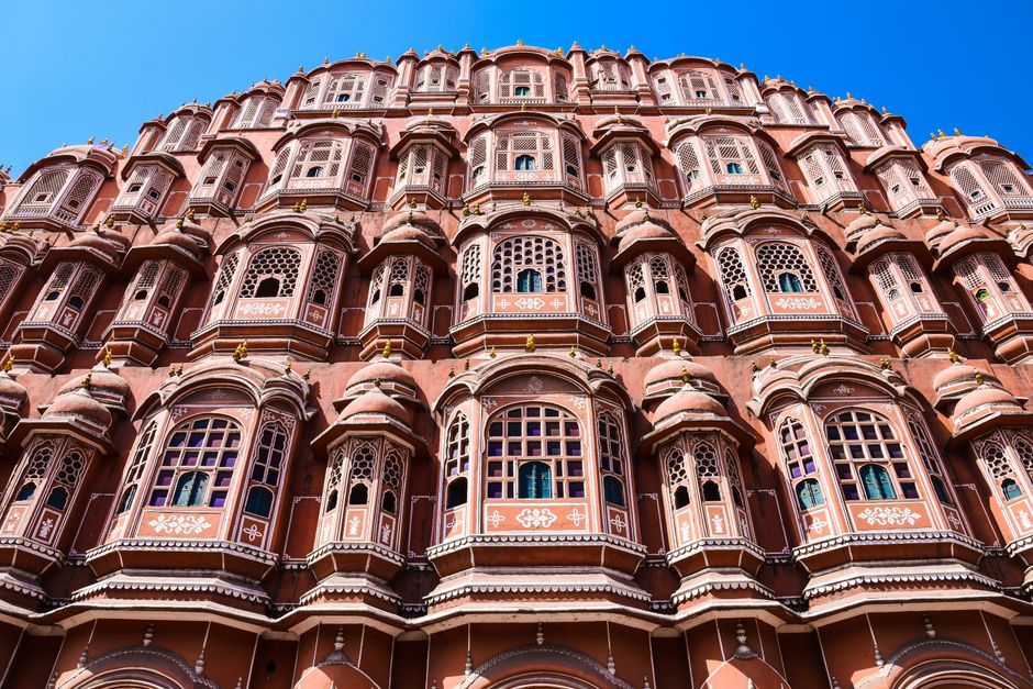 Low angle view of Hawa Mahal's intricate pink sandstone facade against a clear blue sky in Jaipur, India.