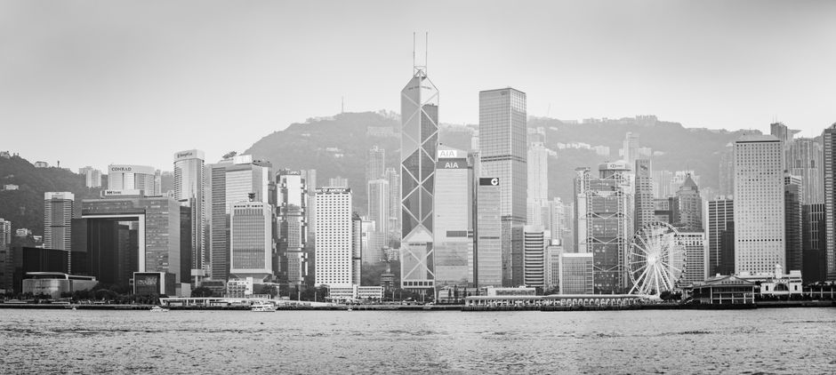 Dramatic view of Hong Kong Island's skyline in grayscale, featuring iconic skyscrapers and Victoria Harbour.